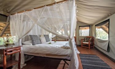 Luxury bed with mosquito netting inside a Meru-style tent at Pungwe Safari Camp